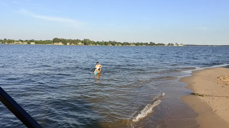 Calm blue water and a sandy beach on Lake Conroe with a woman and child swimming near the shore